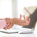 woman at computer holding painful wrist due to carpal tunnel syndrome