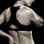 woman athlete with chronic muscle pain holding lower back and shoulder