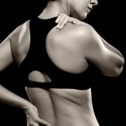 woman athlete with chronic muscle pain holding lower back and shoulder